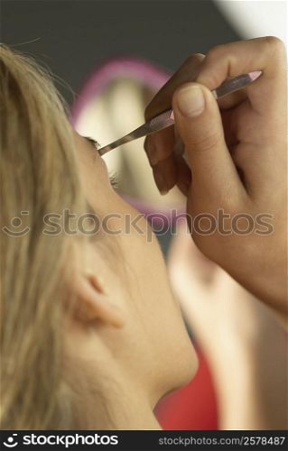 Rear view of a young woman tweezing her eyebrows