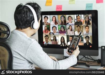 Rear view of Asian man using desktop computer and mobile phone for choosing woman of online dating after Covid-19 pandemic, Social distancing and new normal concept