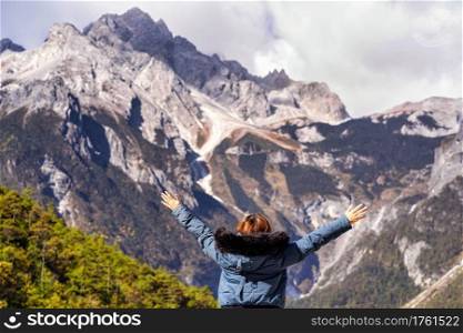 Rear view of Asian woman traveler Raise two hands over the jade dragon snow mountain background at Blue Moon Valley in Jade Dragon Snow Mountain, Lijiang, Yunnan China. Travel and Tourist concept