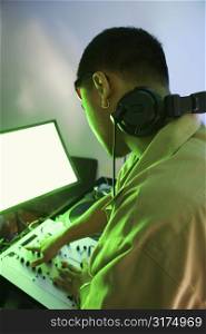 Rear view of Asian young adult male DJ mixing music on equipment.