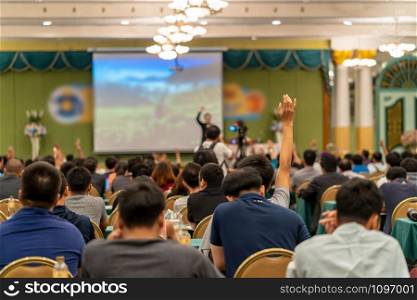 Rear view of Audience showing hand to answer the question from Speaker on the stage in the conference hall or seminar meeting, business and education concept