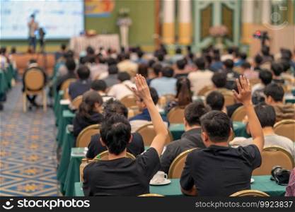 Rear view of Audience showing hand to answer the question from Speaker on the stage in the conference hall or seminar meeting, business and education concept