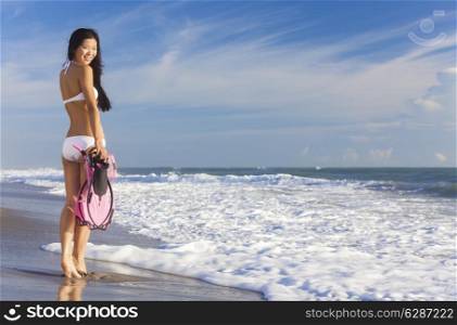 Rear view of beautiful young Asian Chinese woman in bikini with snorkel, mask &amp; flippers on a deserted beach with blue sky