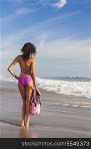 Rear view of beautiful young woman girl in bikini with snorkel, mask &amp; flippers on a deserted beach with blue sky