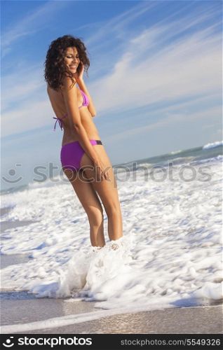 Rear view of beautiful young woman in bikini standing in the surf waves on a deserted tropical beach with blue sky