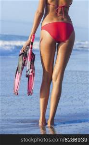 Rear view of beautiful young woman in red bikini with snorkel, mask &amp; flippers on a deserted beach with blue sky