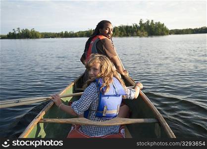 Rear view of blond girl and Africian American man rowing in a canoe at Lake of the Woods, Ontario