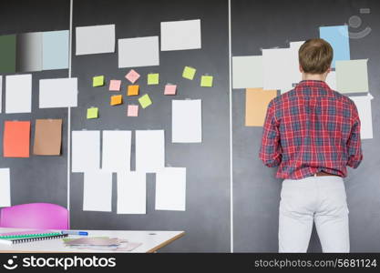 Rear view of businessman analyzing documents on wall at creative office