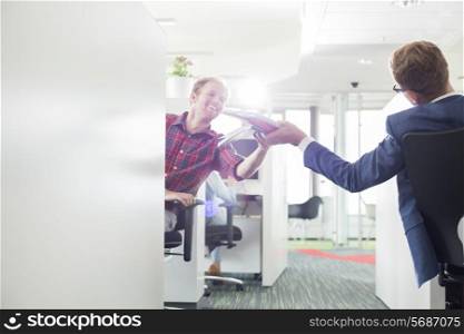 Rear view of businessman giving files to colleague in creative office