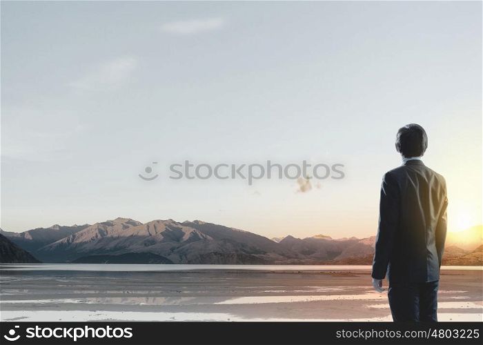 Rear view of businessman look at sunrise above mountain. Facing new day