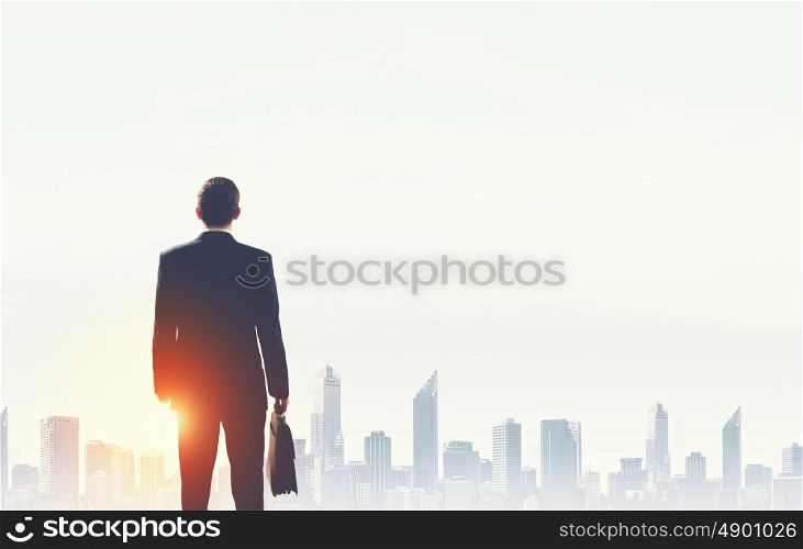 Rear view of businessman looking at sunset above city. New day