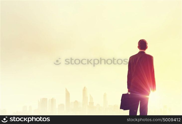 Rear view of businessman looking at sunset above city. New day