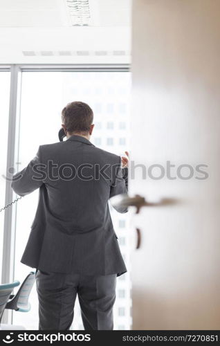 Rear view of businessman talking on telephone seen through cabin doorway in office