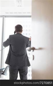 Rear view of businessman talking on telephone seen through cabin doorway in office