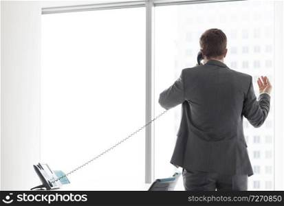 Rear view of businessman talking on telephone while looking through window in office