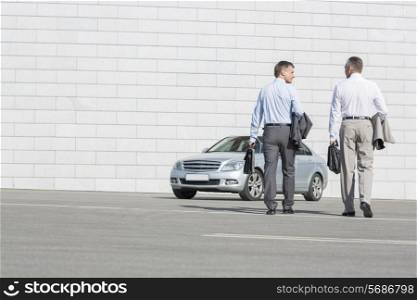 Rear view of businessmen carrying briefcases while walking towards car on street