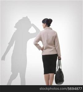 Rear view of businesswoman looking at her shadow dancing over gray background