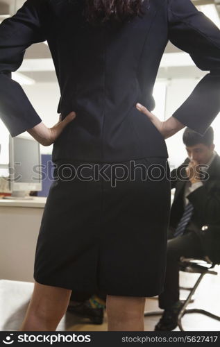 Rear view of businesswoman with her hands on hips confronting a coworker