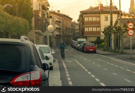Rear view of car parked beside asphalt street in town with blurred people ride a bicycle for exercise in spring morning. Blurred traffic sign of city limit speed 30 km/hr. Old building in the city.