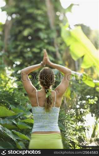 Rear view of Caucasian mid-adult woman holding arms overhead in yoga position.