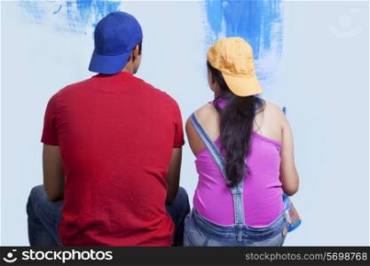 Rear view of couple sitting in front of incomplete wall painting