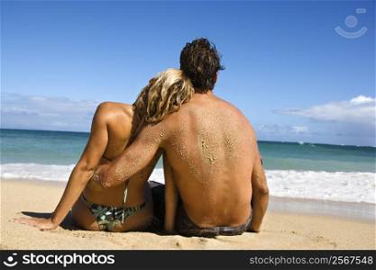 Rear view of couple sitting on Maui, Hawaii beach with woman leaning head on man&acute;s shoulder.