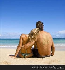 Rear view of couple sitting on Maui, Hawaii beach with woman leaning head on man&acute;s shoulder.
