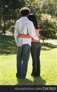 Rear view of couple standing in park with arms around eachother.