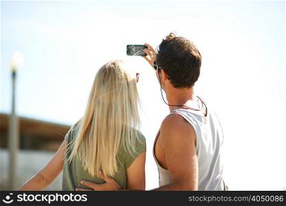 Rear view of couple taking smartphone selfie at Venice Beach, Los Angeles, California, USA