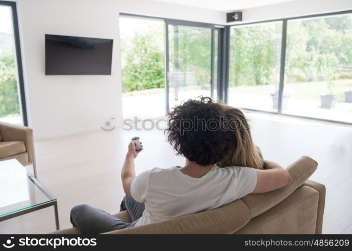 Rear view of couple watching television in living room their luxury home