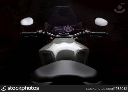 Rear view of custom grey caferacer motorbike with its headlight on, on dark background.. Custom caferacer motorbike on dark background with its headlight on.