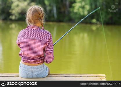 Rear view of cute girl sitting at bank and fishing