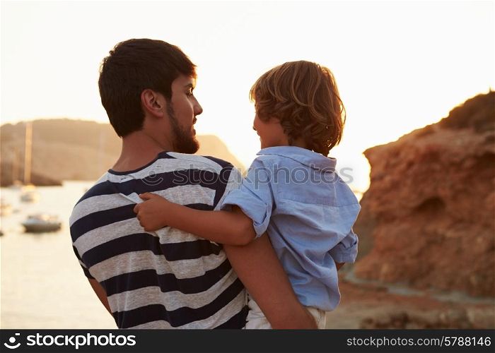Rear View Of Father And Son Watching Sunset Over Harbour