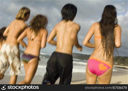 Rear view of five people running on the beach