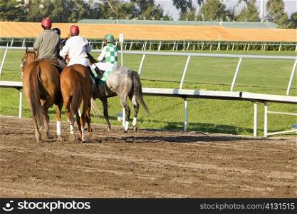 Rear view of four jockeys riding horses on a horseracing track