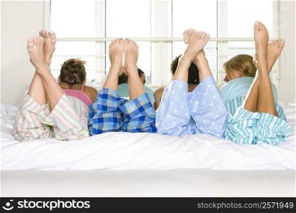 Rear view of four young women lying down side by side on a bed