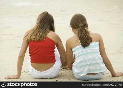 Rear view of girl and a teenage girl sitting together on the beach