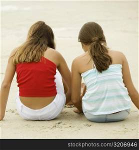 Rear view of girl and a teenage girl sitting together on the beach
