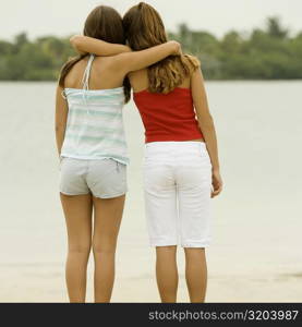 Rear view of girl and a teenage girl standing with their arms around each other on the beach