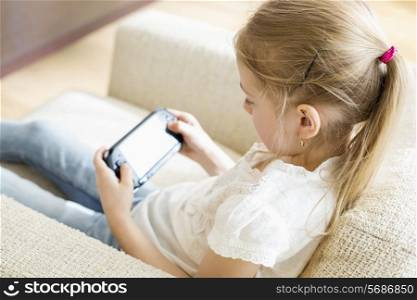 Rear view of girl playing hand-held video game at home