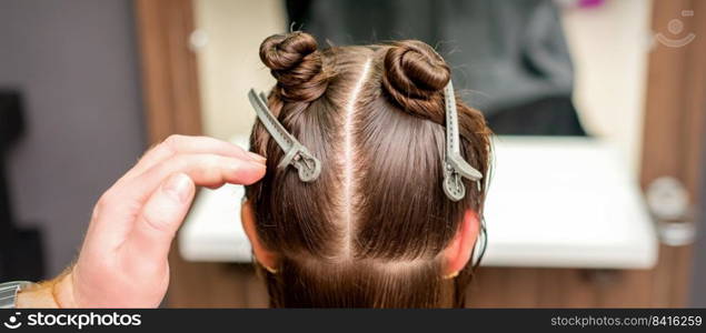 Rear view of hand of hairdresser doing haircut of young woman with hair clips on her hair in hair salon. Hair clips on hair of young woman