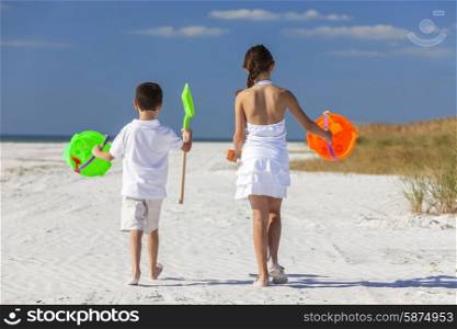 Rear view of happy children, boy girl, brother and sister having fun playing in the sand on a beach with bucket and spade