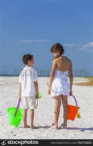 Rear view of happy children, boy girl, brother and sister having fun playing in the sand on a beach with bucket and spade