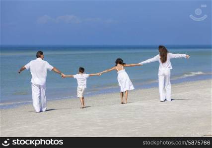 Rear view of happy family of mother, father and two children, son and daughter, walking holding hands and having fun in the sand on a sunny beach