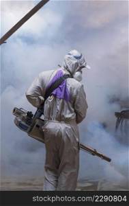 Rear view of healthcare worker using fogging machine spraying chemical to eliminate mosquitoes inside of the old storage in vertical frame