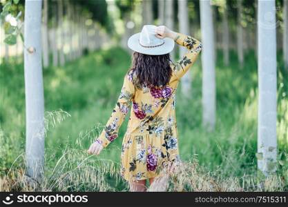 Rear view of hiker young woman, wearing flowered dress, hiking in the countryside.. Young woman, wearing flowered dress, between trees.