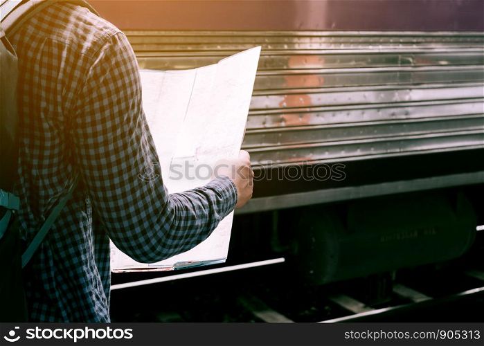 Rear view of hipster man standing on train station with looking map paper.