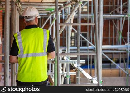 Rear view of male builder construction worker on building site wearing hard hat and hi-vis vest