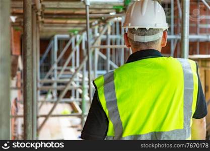 Rear view of male builder construction worker or builder on building site wearing hard hat and hi-vis vest