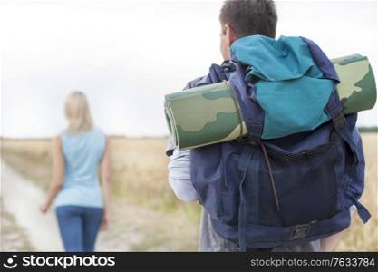 Rear view of male hiker carrying backpack with woman walking in foreground on field